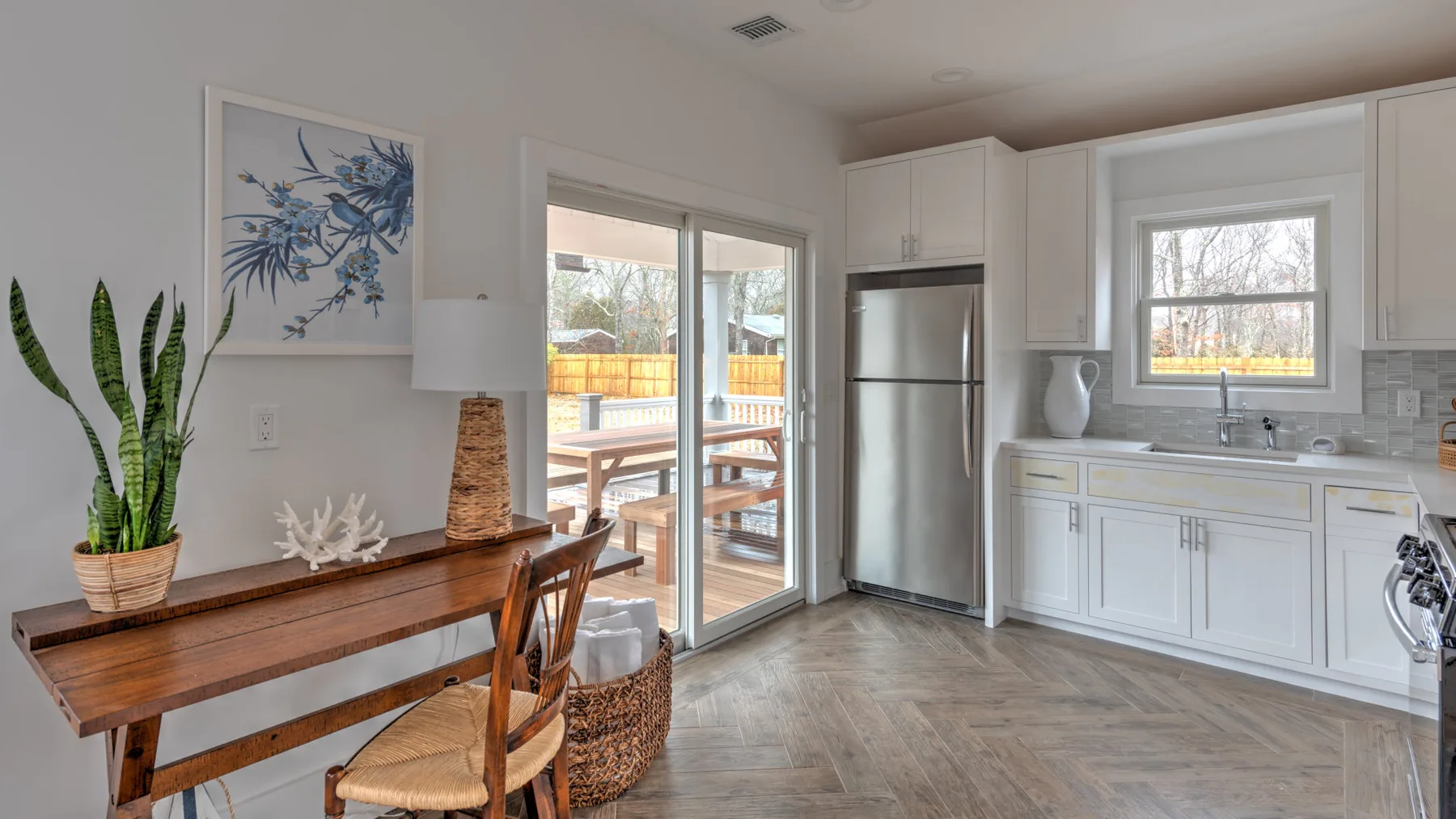 Una cocina y comedor luminosos con gabinetes blancos y una mesa de madera.