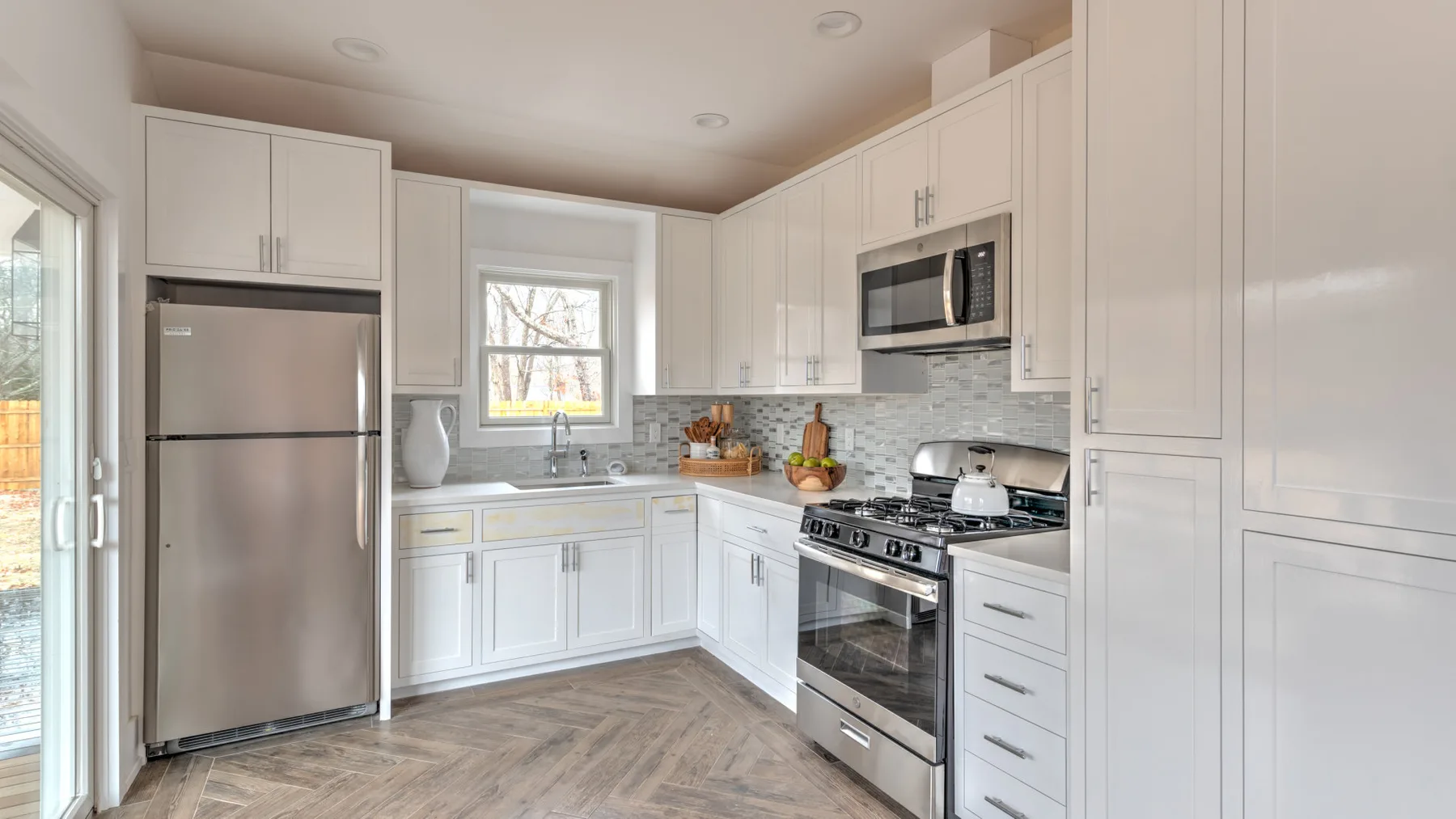 Una cocina luminosa con gabinetes blancos, electrodomésticos de acero inoxidable y una ventana central.