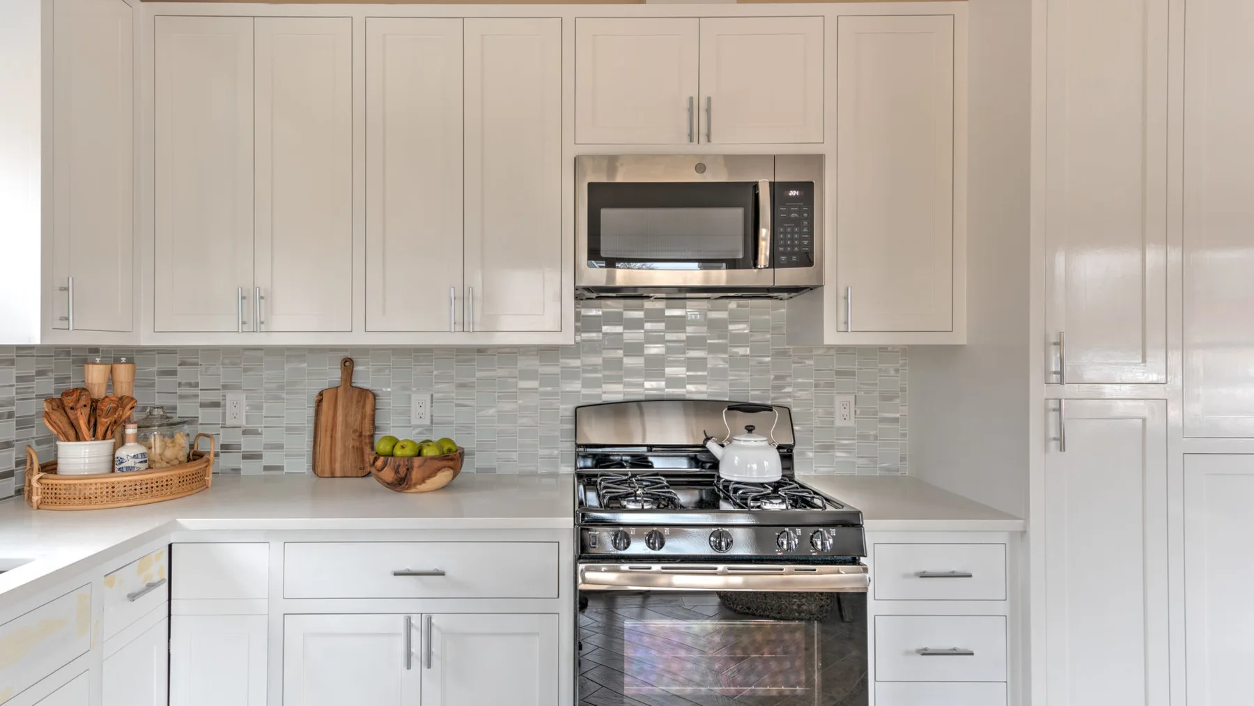 Una cocina luminosa con gabinetes blancos, un salpicadero de azulejos y una estufa.