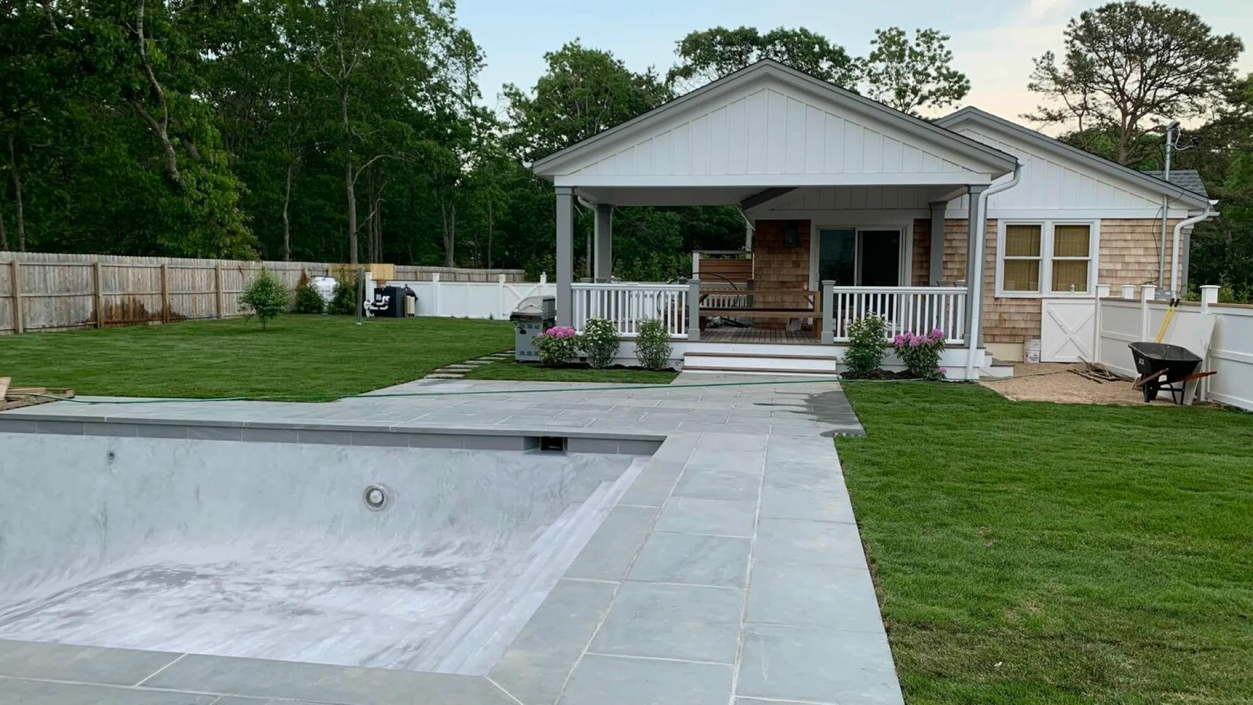 Una casa con patio cubierto da a una piscina vacía y un césped.