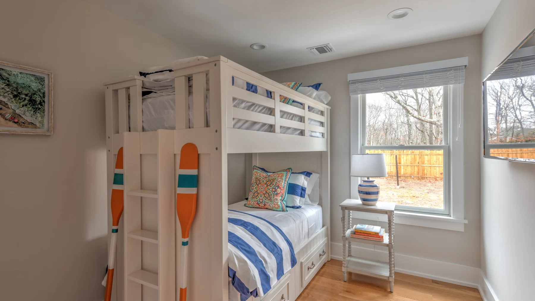 Una litera con ropa de cama a rayas azules está junto a una ventana luminosa.