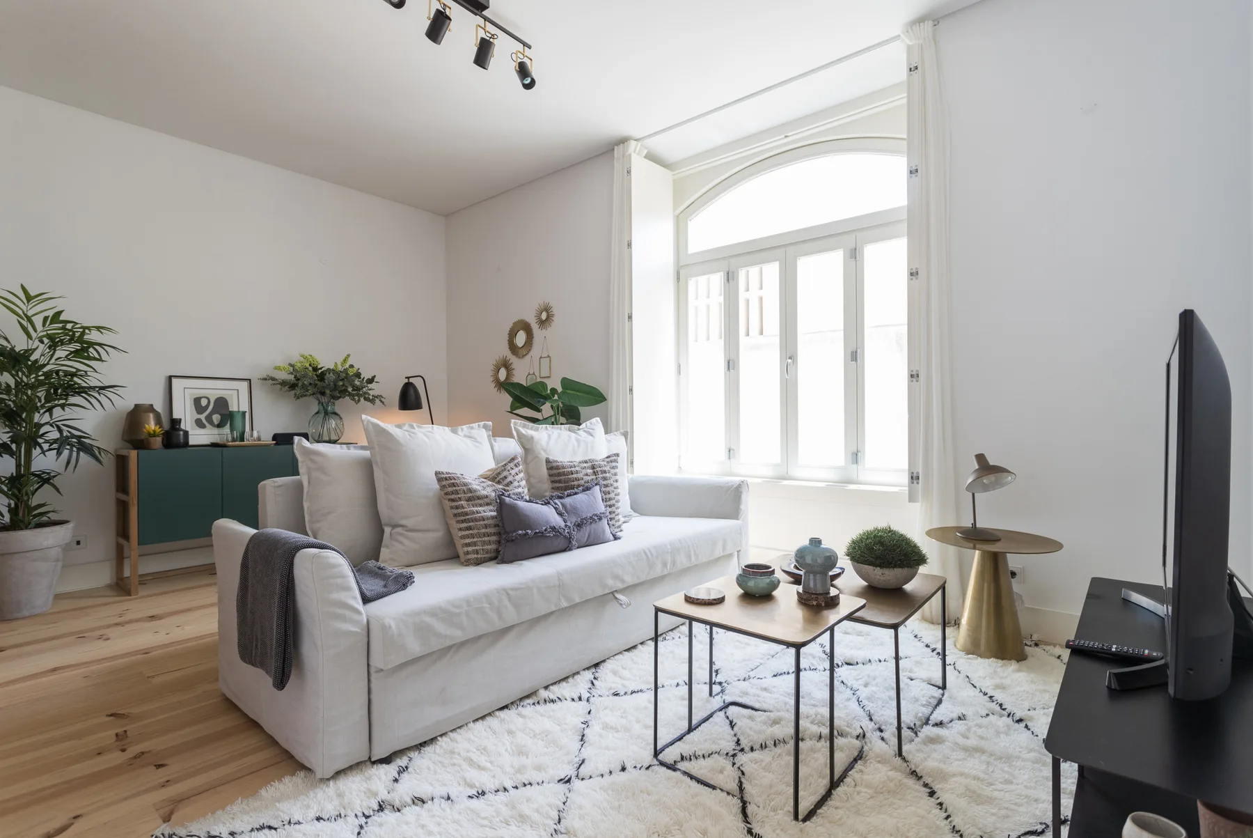 Una sala de estar luminosa con asientos blancos, una mesa de centro y ventanas grandes.