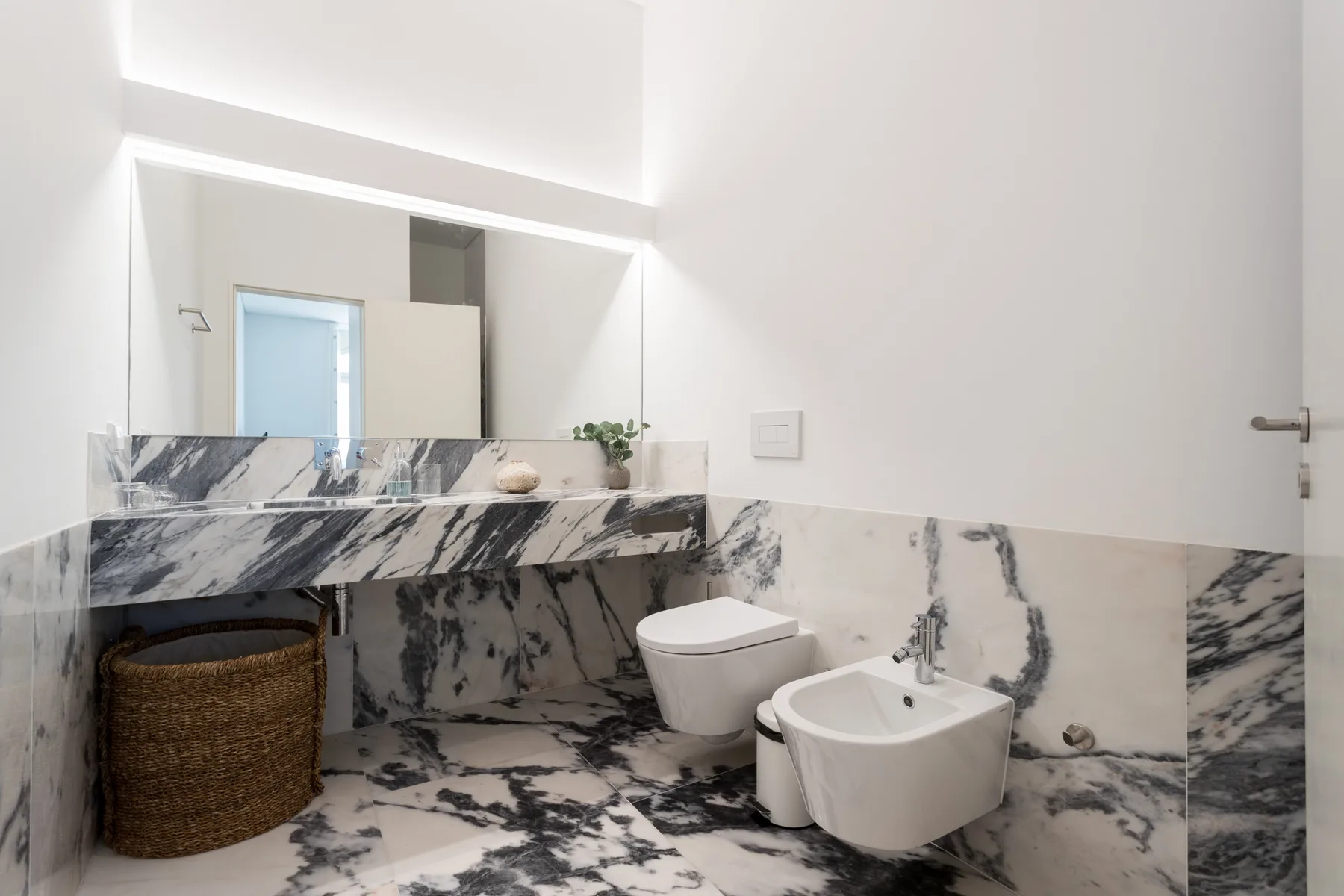 A bathroom with a large mirror above the sink and marble-patterned surfaces.