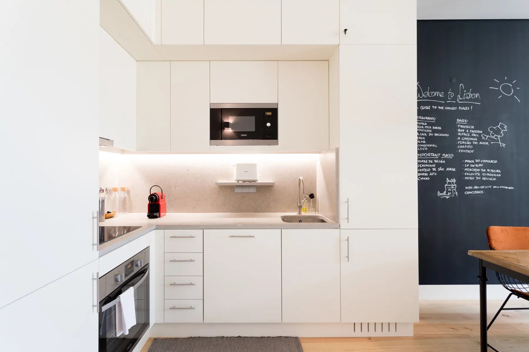 A modern kitchen with white cabinets, a built-in oven, and a dark chalkboard wall.