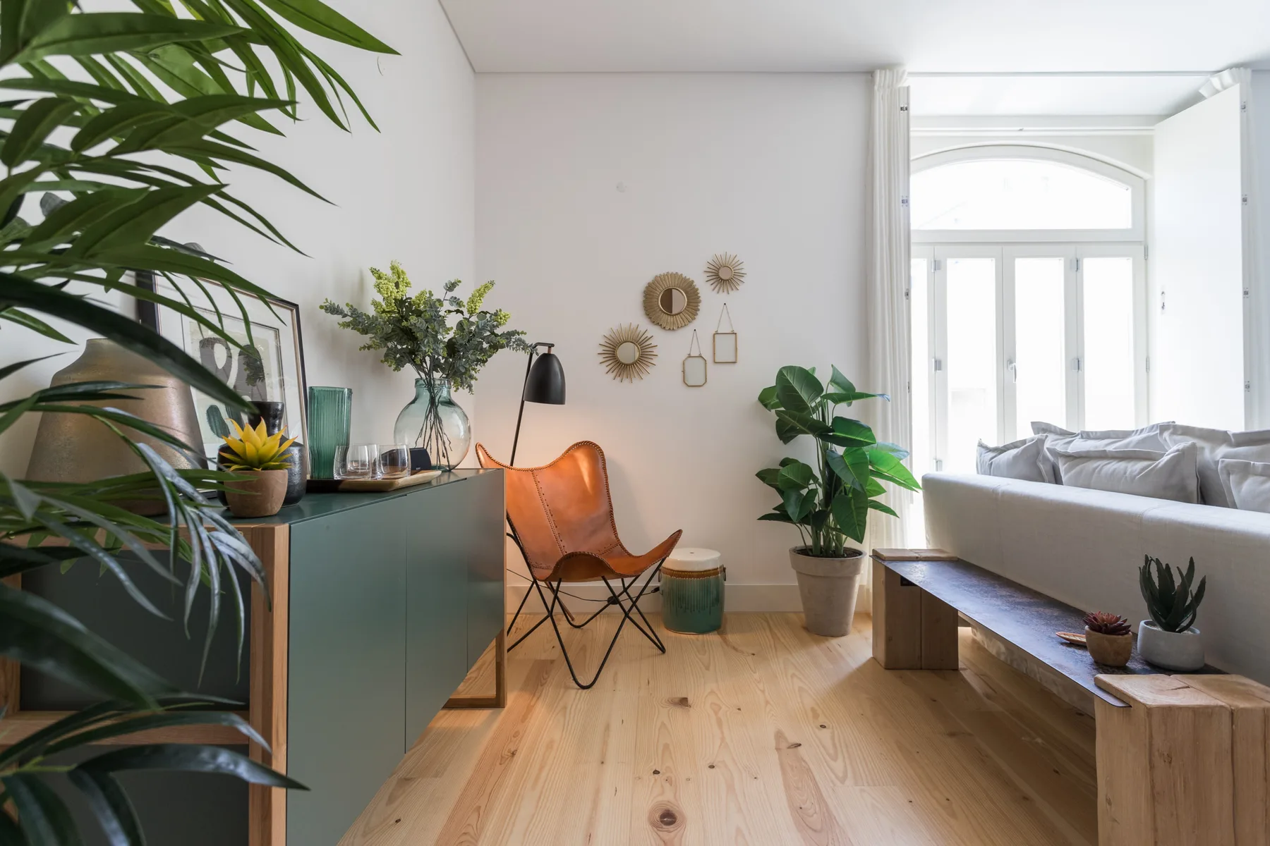 A bright living room with a teal cabinet, a lounge chair, and a long wooden table.