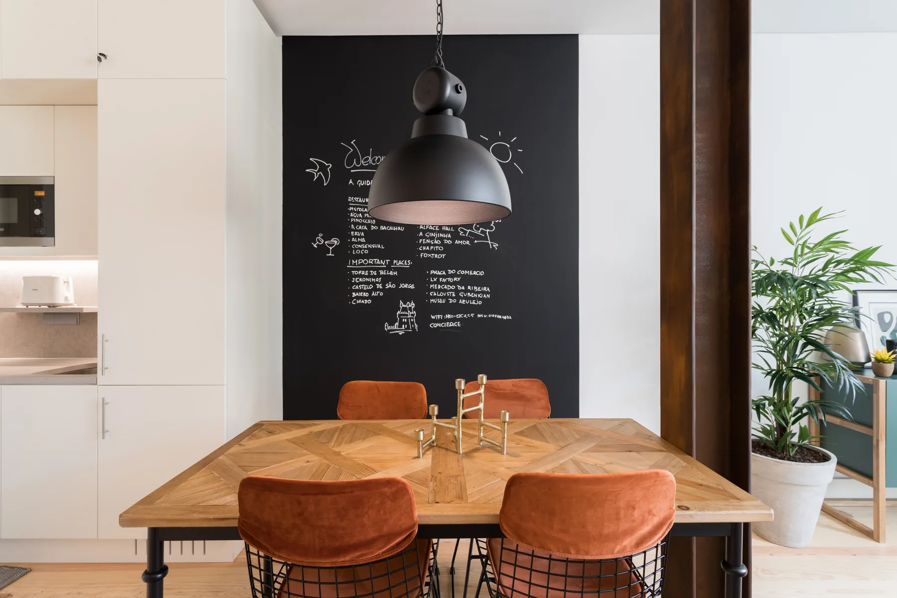 A dining area with a wooden table, orange seating, and a chalkboard wall.