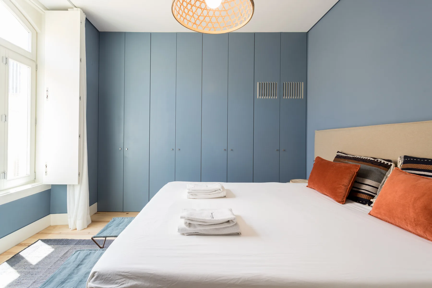 A bedroom with a neatly made bed, folded towels, and blue built-in cabinets.