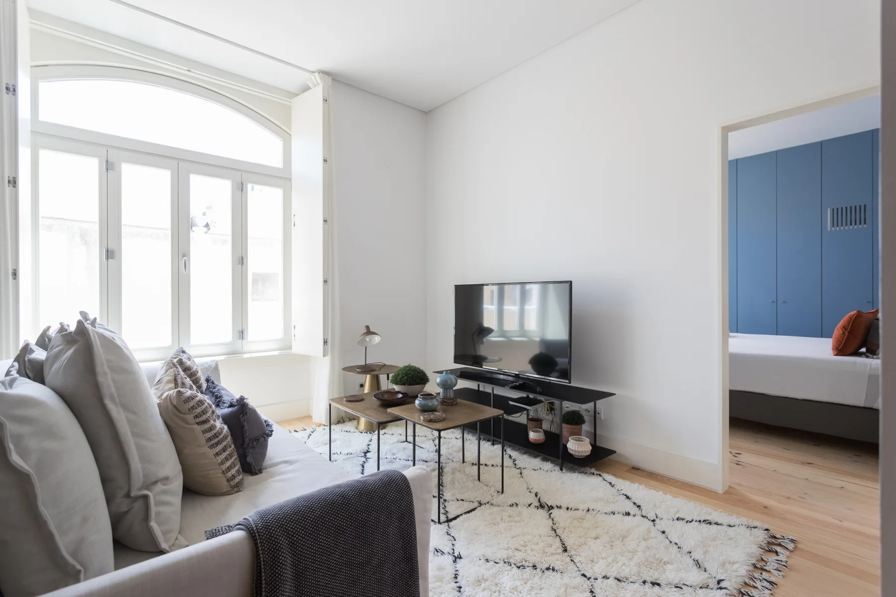 Una sala luminosa con asientos, un televisor y ventanas grandes.