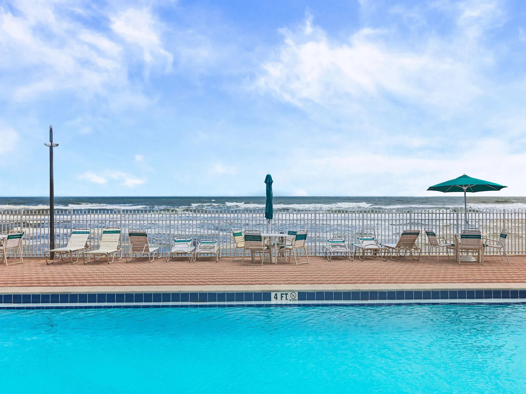 A swimming pool overlooks the ocean, with lounge seating along the deck.