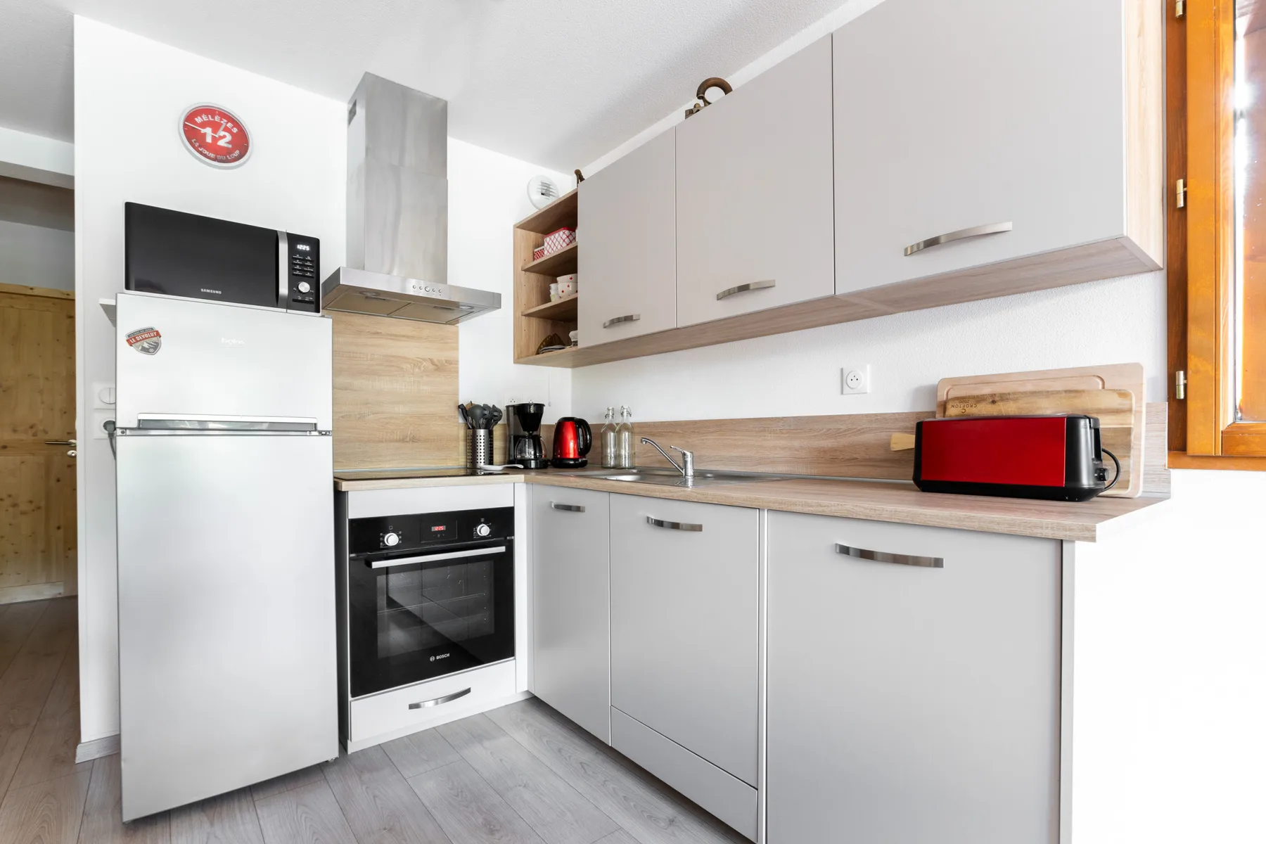A bright kitchen with light cabinets, a refrigerator, and countertop appliances.