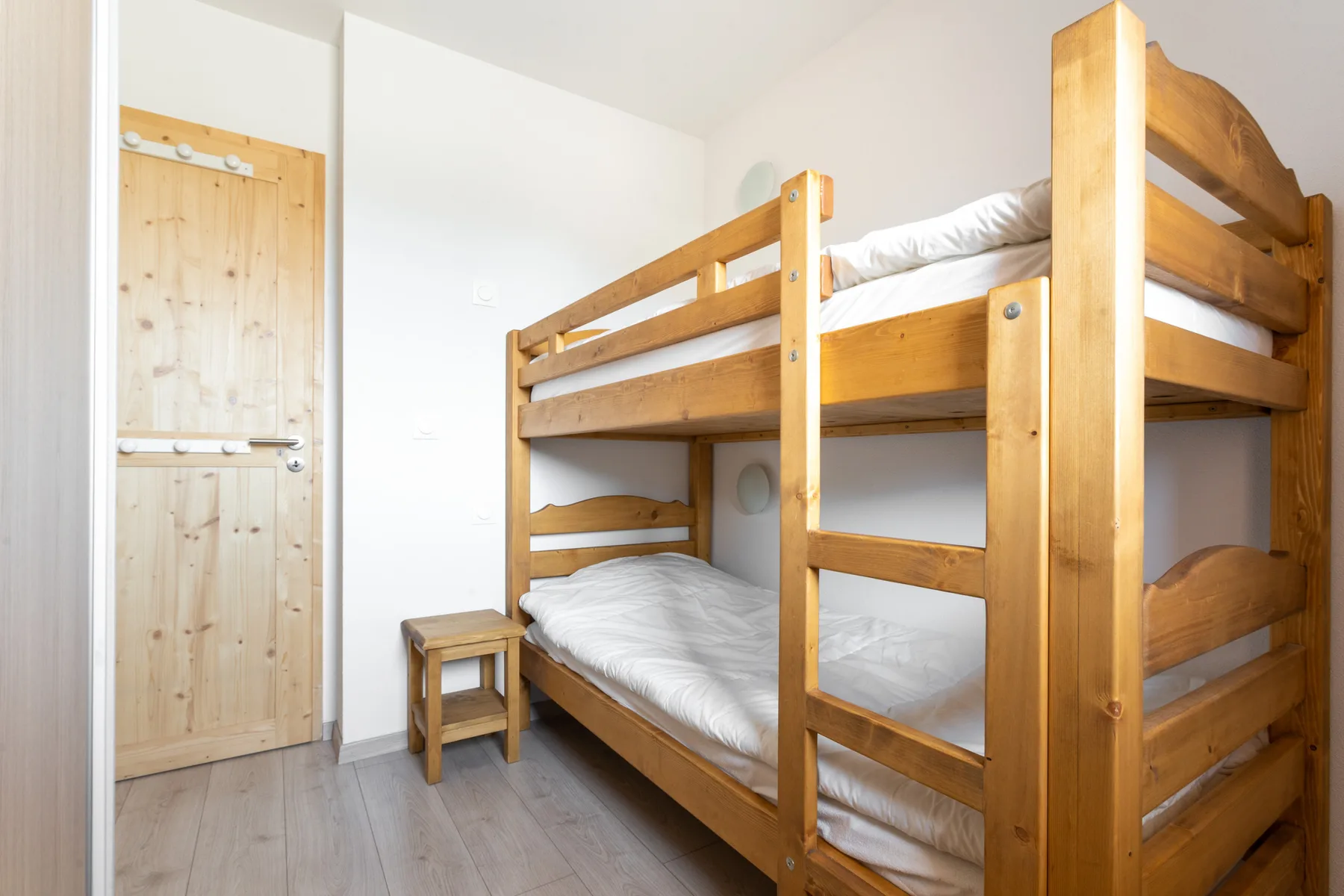 A bedroom with a wooden bunk bed and a small bedside table.
