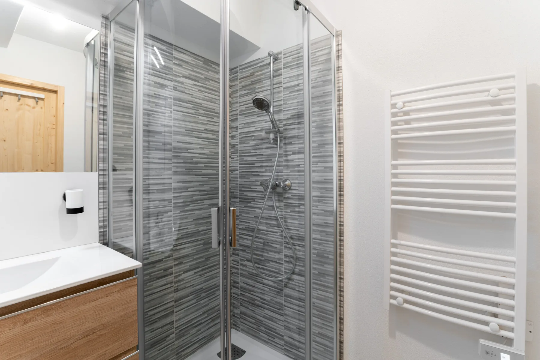 A bathroom with a glass shower and a wall-mounted towel radiator.