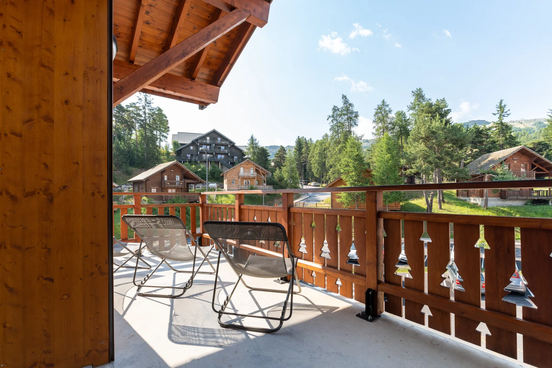 A covered wooden balcony with seating overlooks trees and nearby buildings.