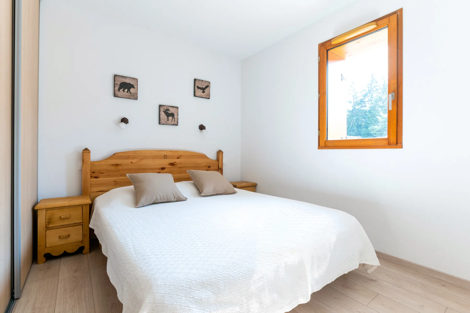 A bedroom with a wooden bed, white bedding, and a bright window.