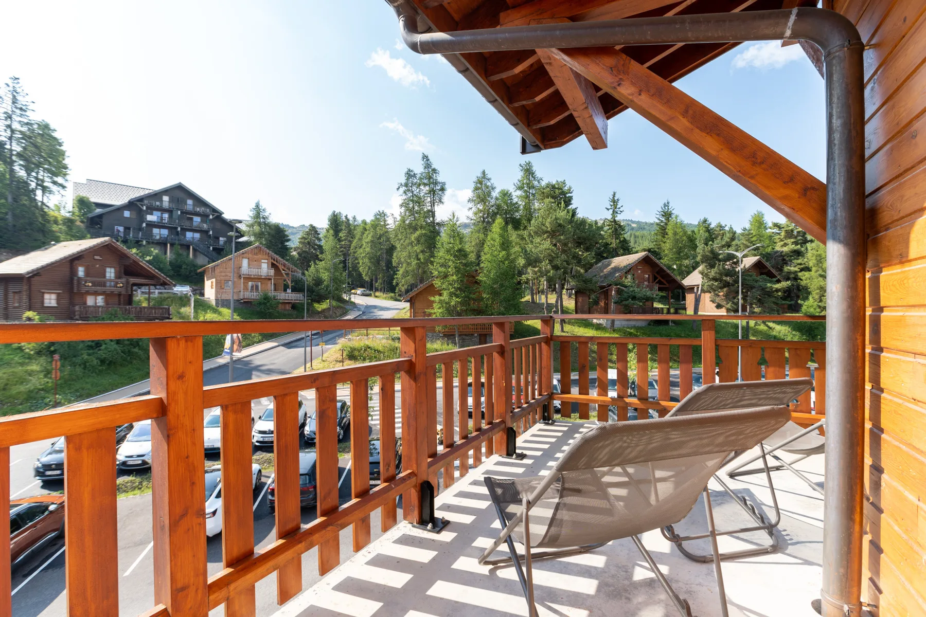 A wooden balcony with lounge seating overlooks a wooded neighborhood.