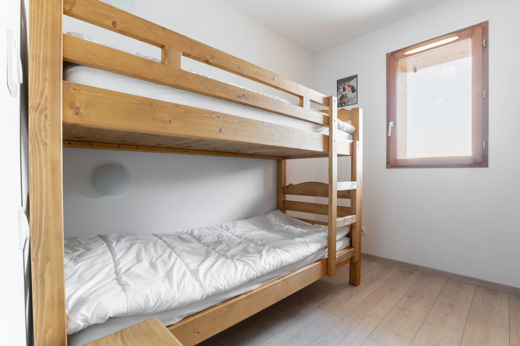 A bunk bed with white bedding sits beside a sunlit window.