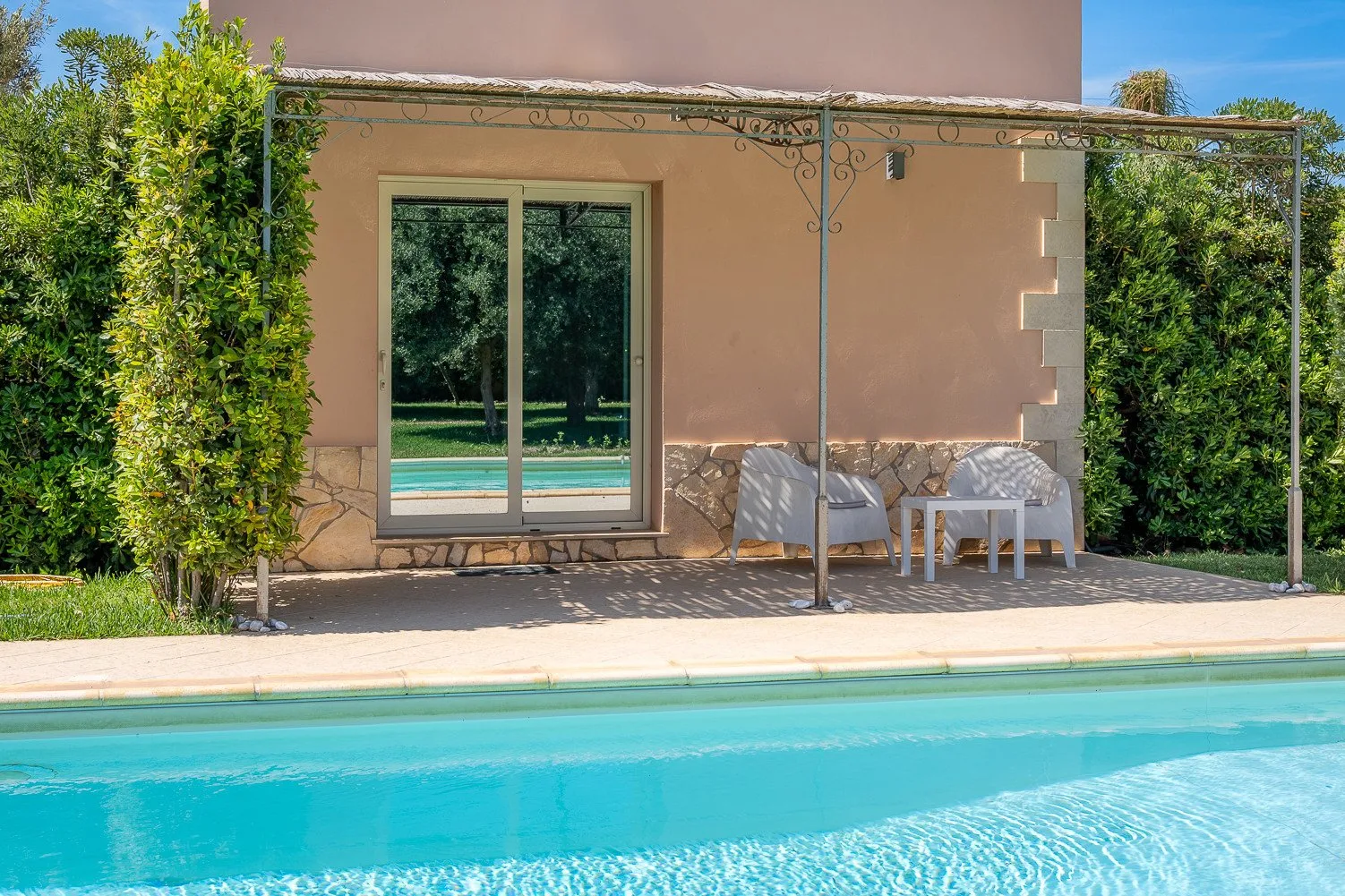 Una piscina bordea un patio sombreado con asientos al aire libre junto a un edificio.