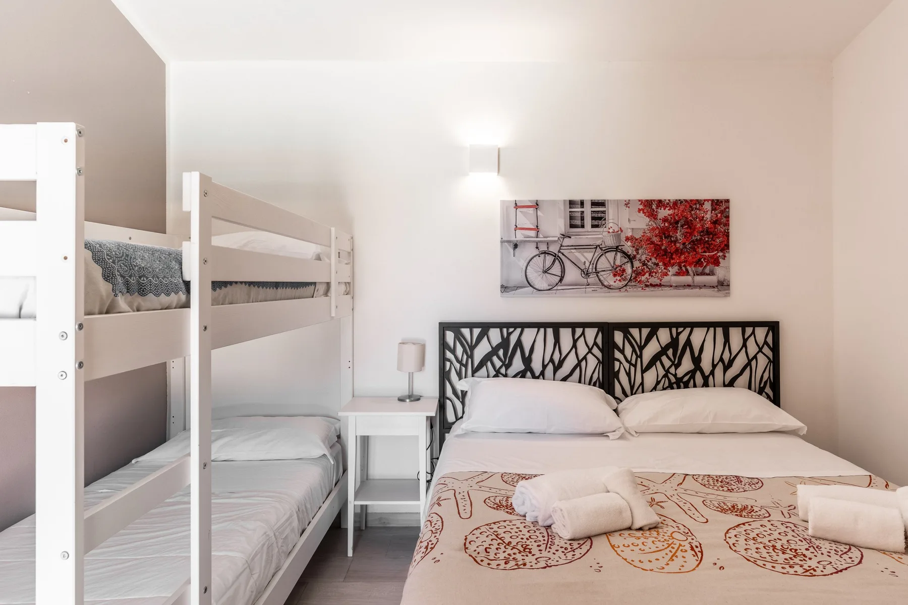 Un dormitorio con literas junto a una cama doble y un cuadro enmarcado de bicicletas.