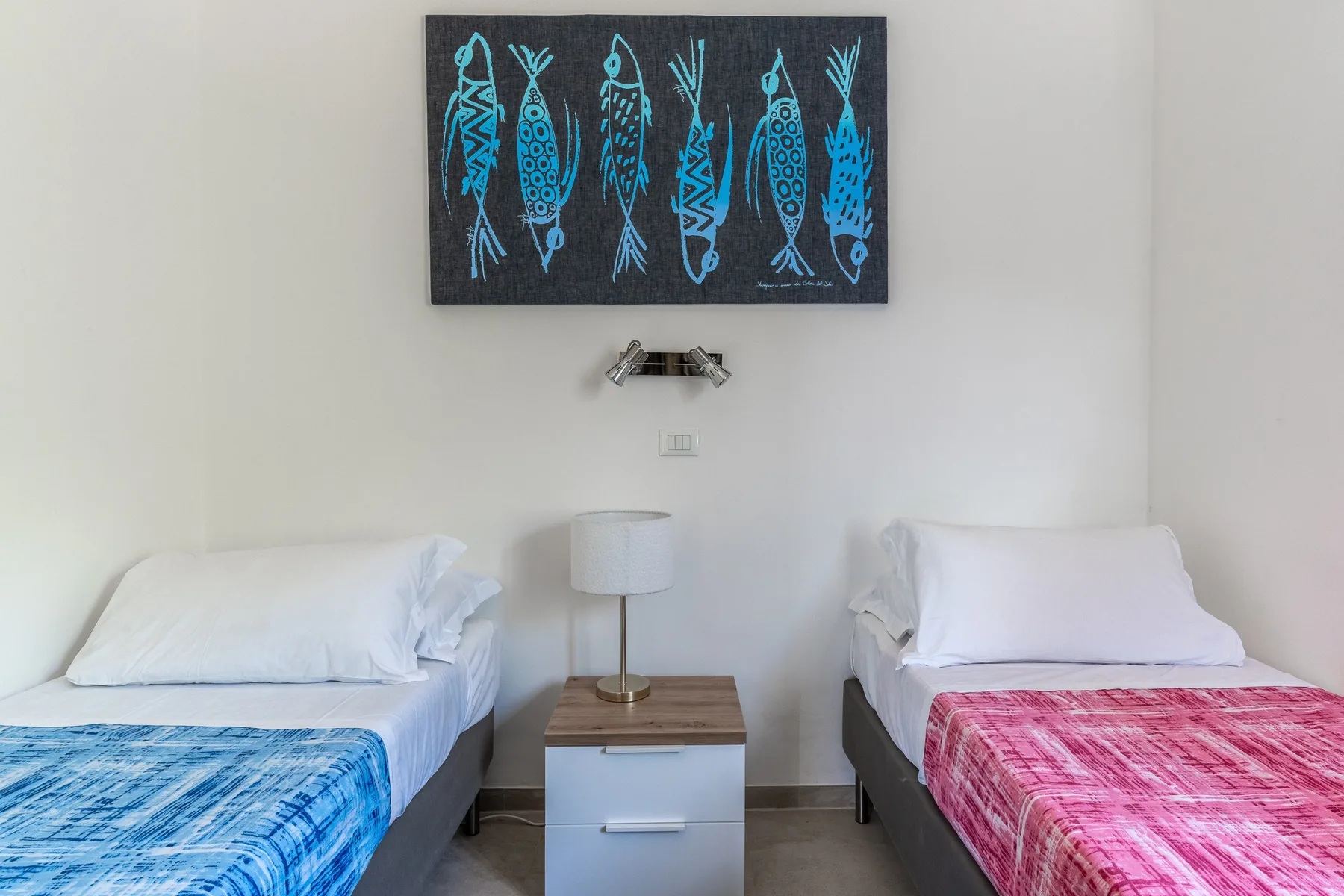 Un dormitorio con dos camas individuales y una mesita bajo un cuadro de peces.