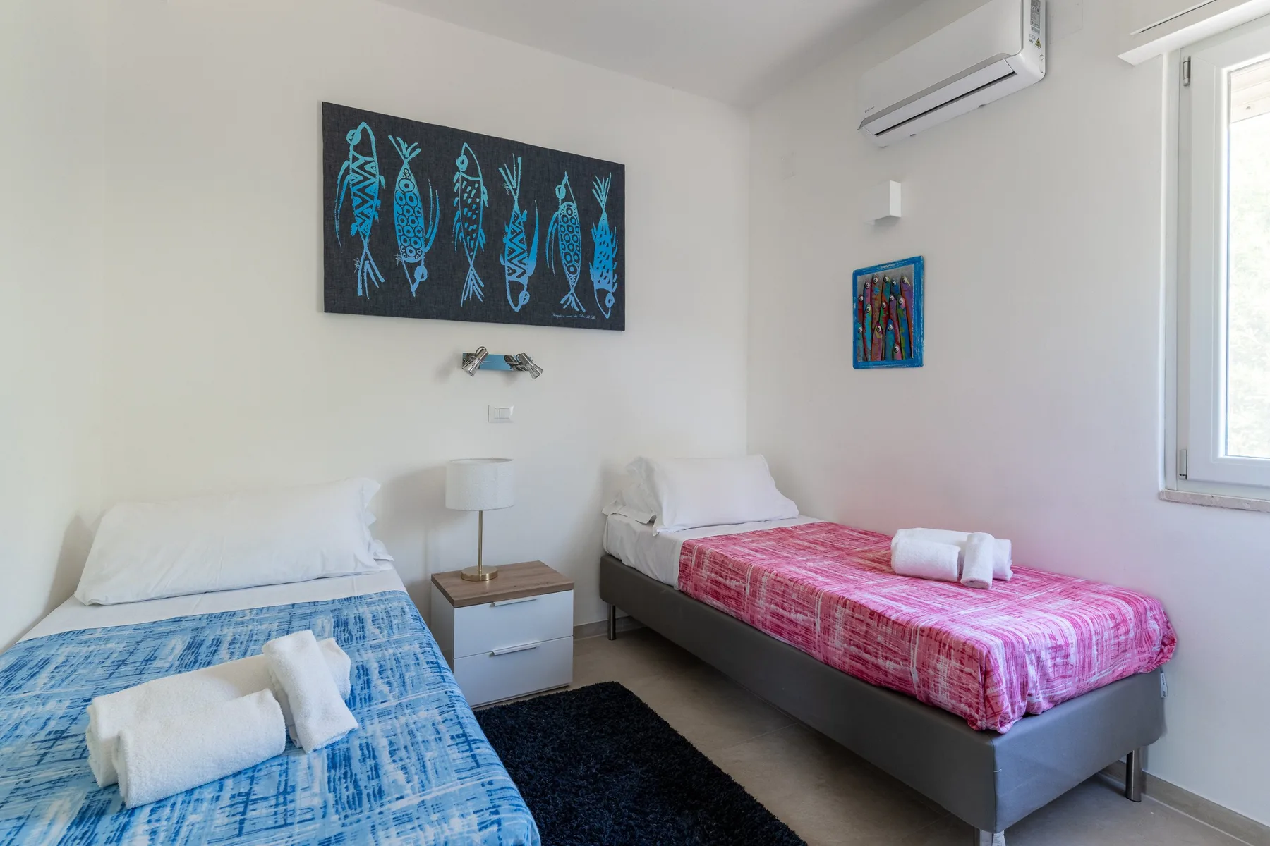 Un dormitorio luminoso con dos camas, ropa de cama colorida y arte en las paredes.