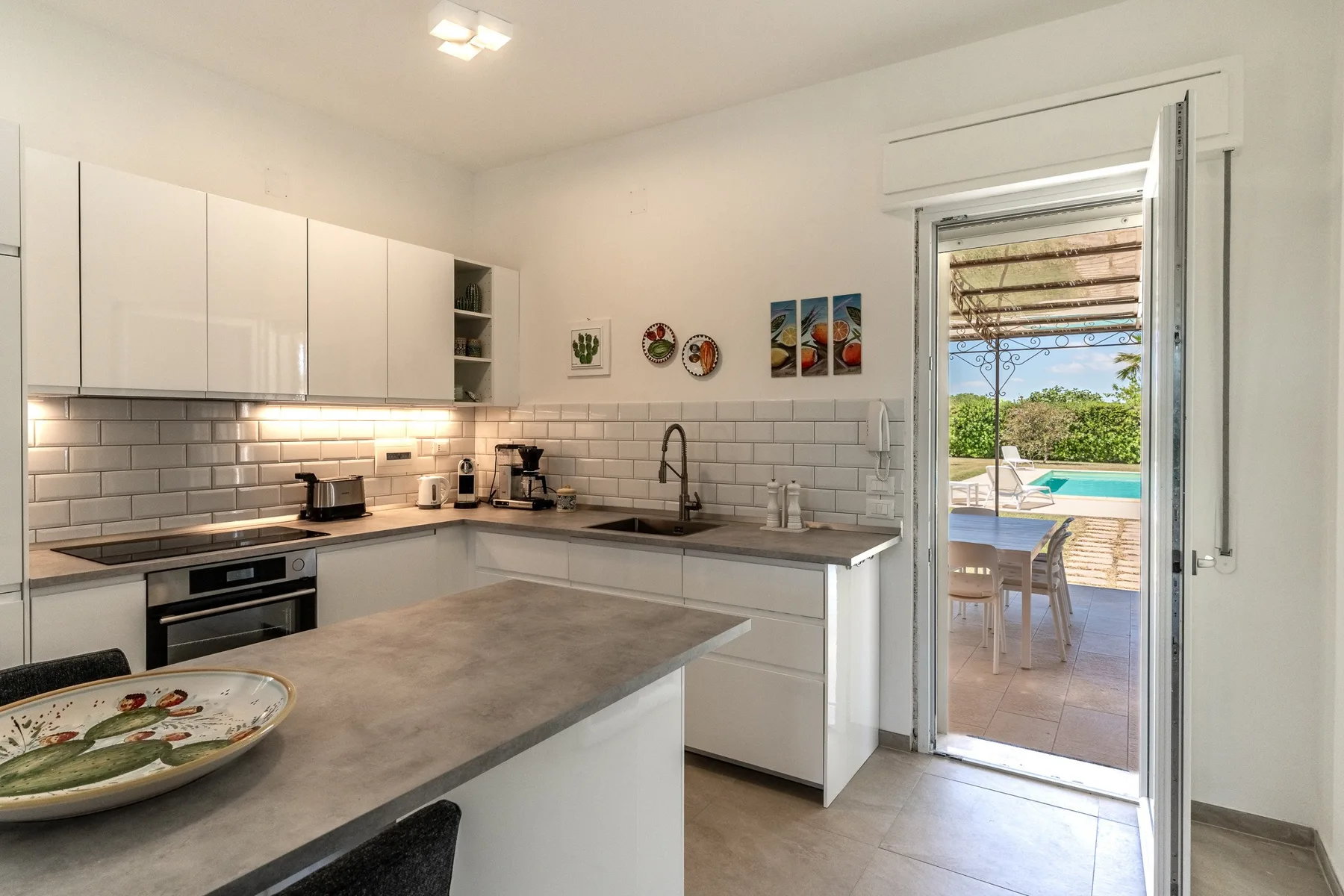 Una cocina luminosa con una encimera central y una puerta abierta al patio.