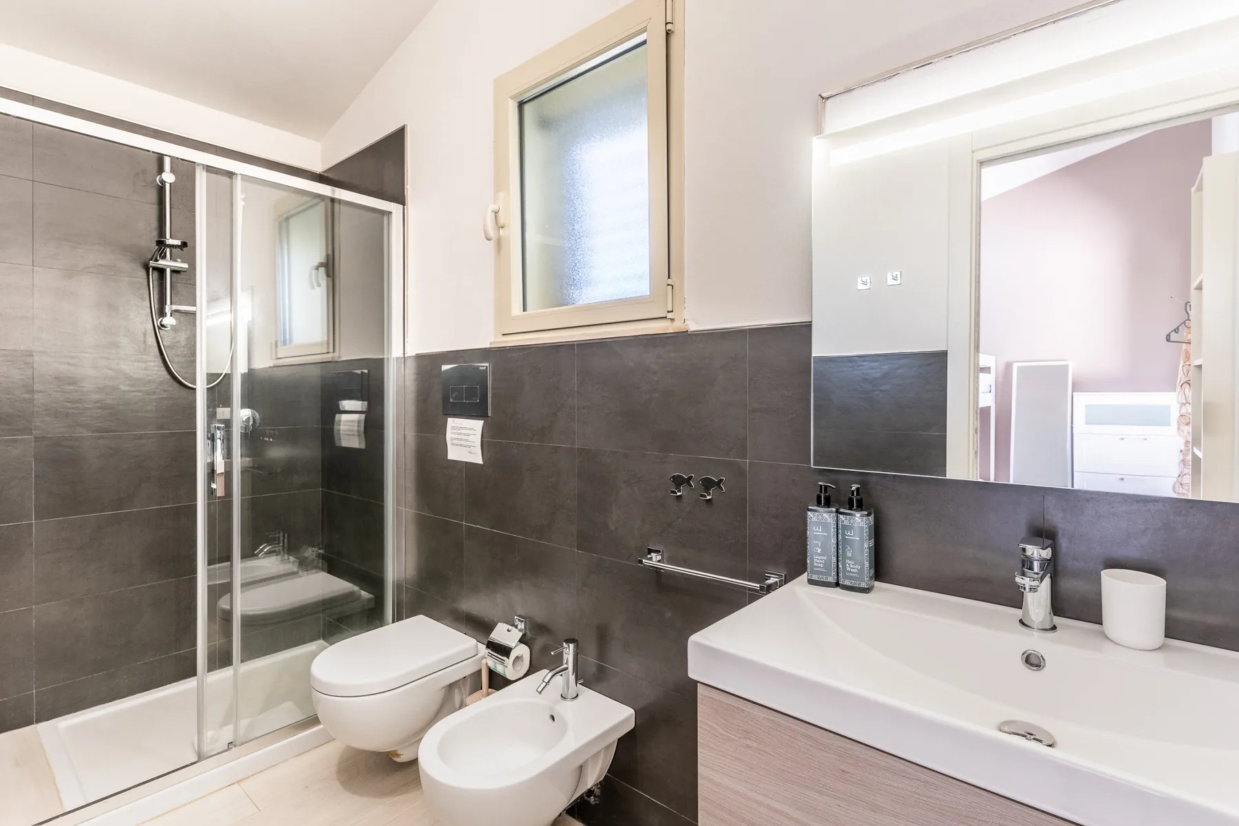 Un baño con ducha de vidrio, inodoro, bidé y un amplio lavabo.