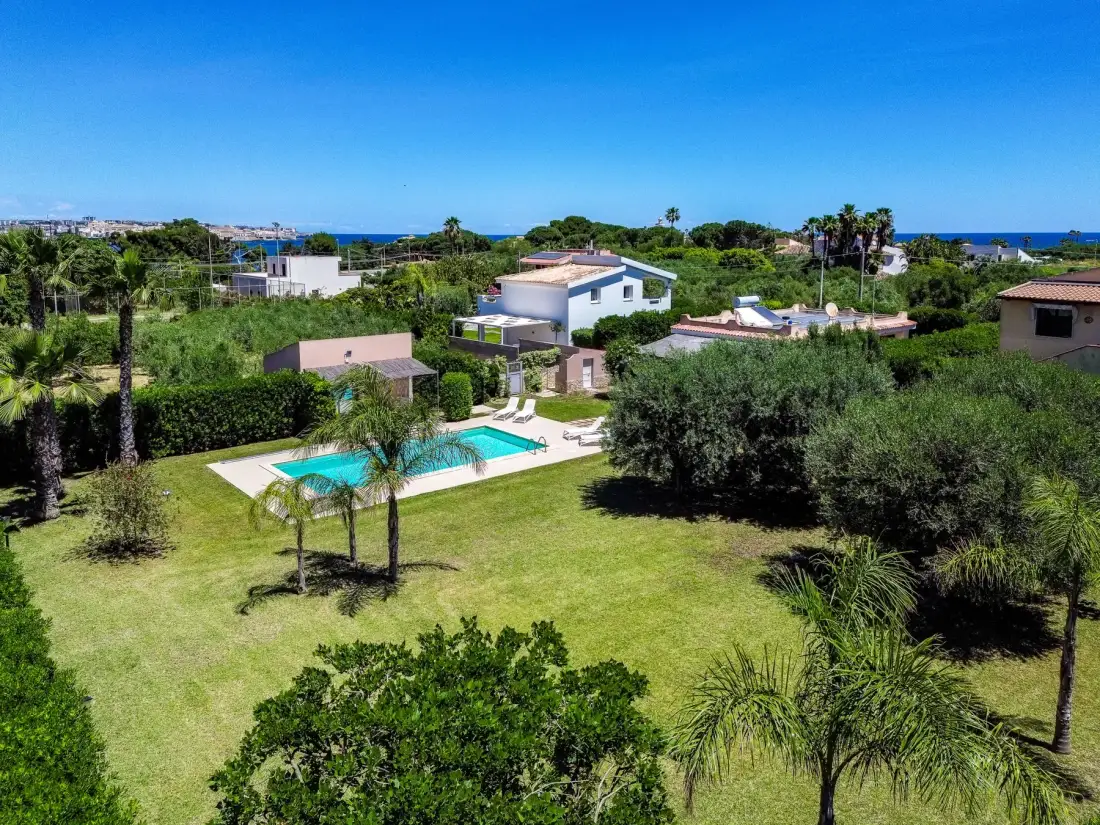 Una propiedad residencial ajardinada con piscina y el mar visible a lo lejos.