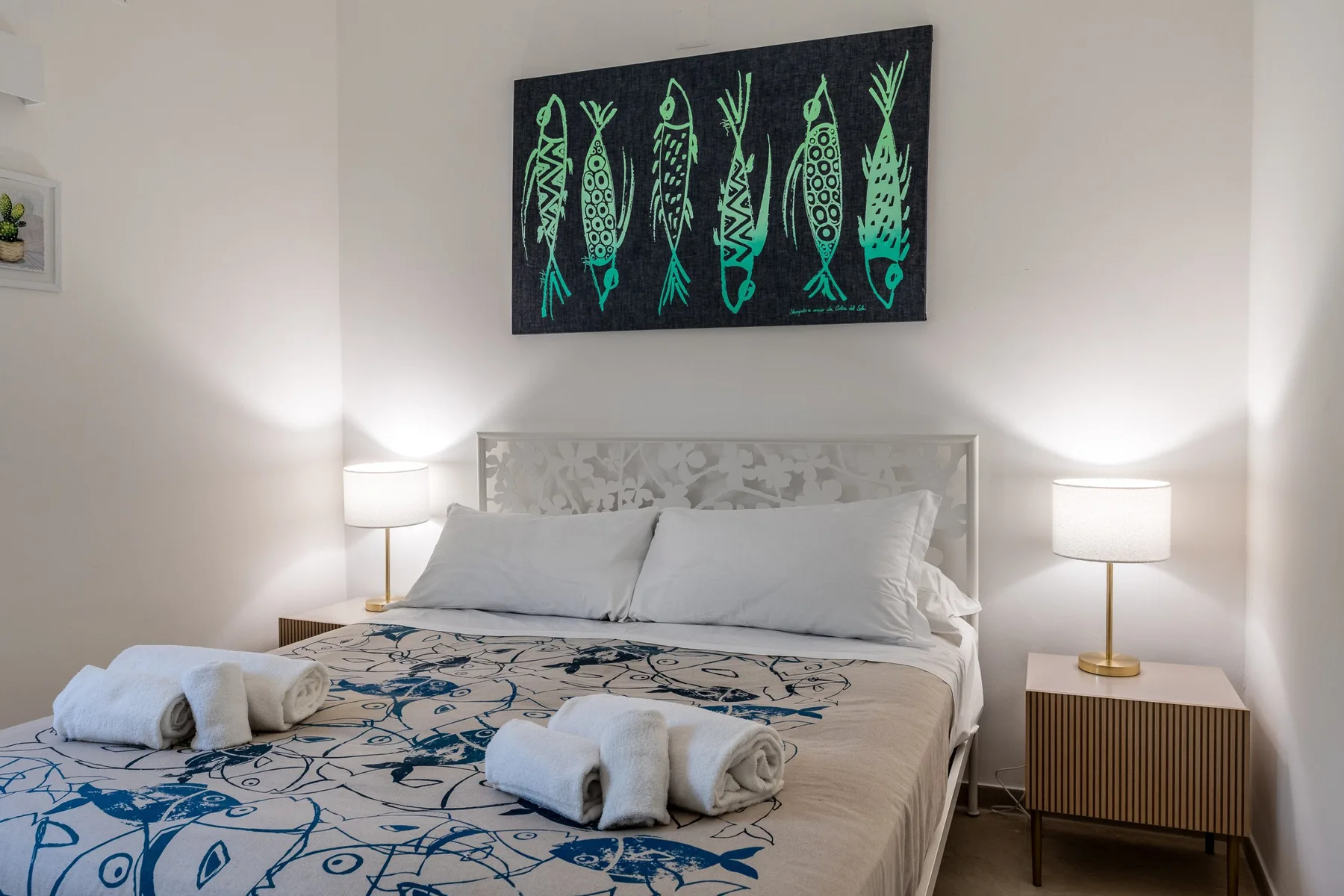 Un dormitorio con una cama tendida y arte de peces sobre el cabecero.