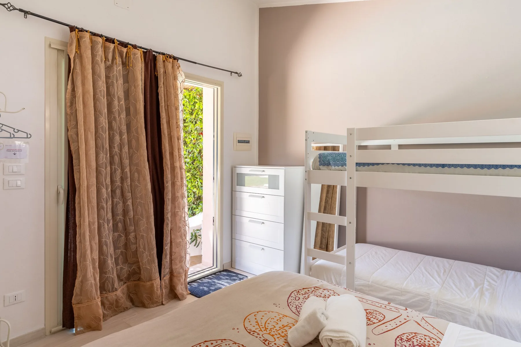 Un dormitorio con literas, una cómoda y una puerta abierta con cortinas.