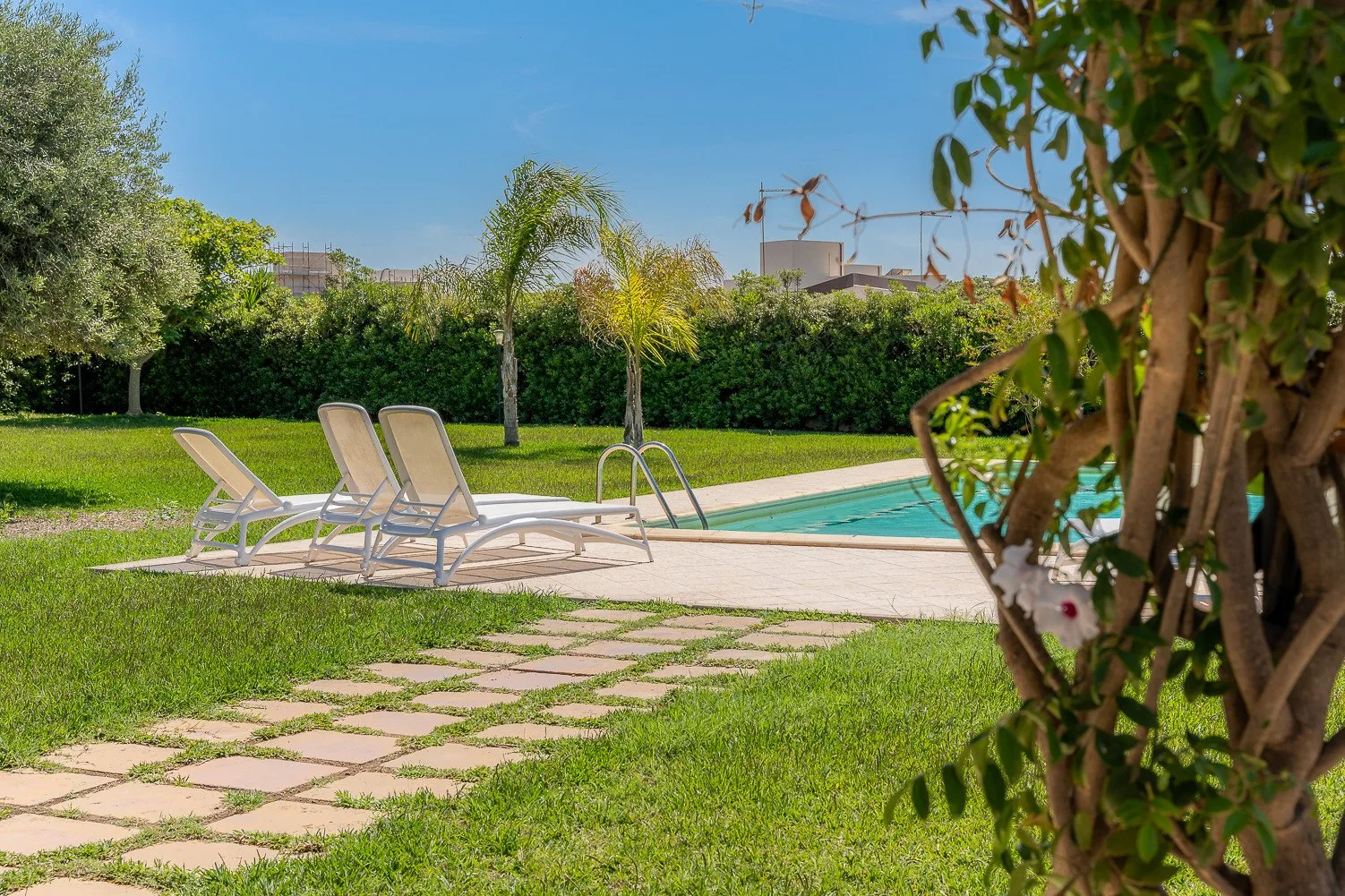 Una piscina al aire libre con asientos reclinables junto a un césped verde.