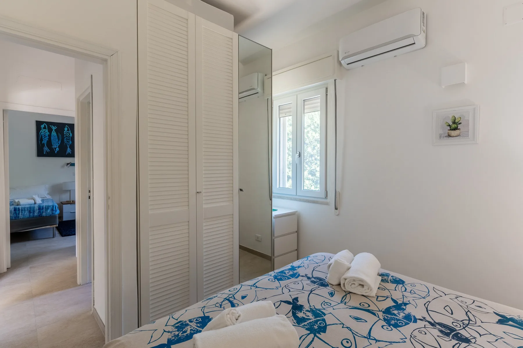 Un dormitorio luminoso con una colcha estampada azul y una ventana.