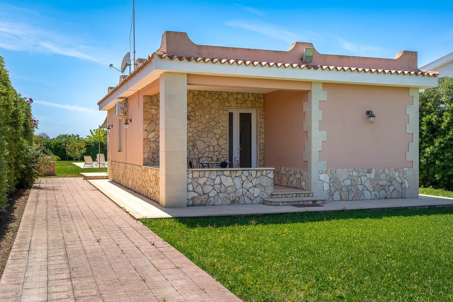 Una casa pequeña con entrada cubierta, camino pavimentado y césped verde.