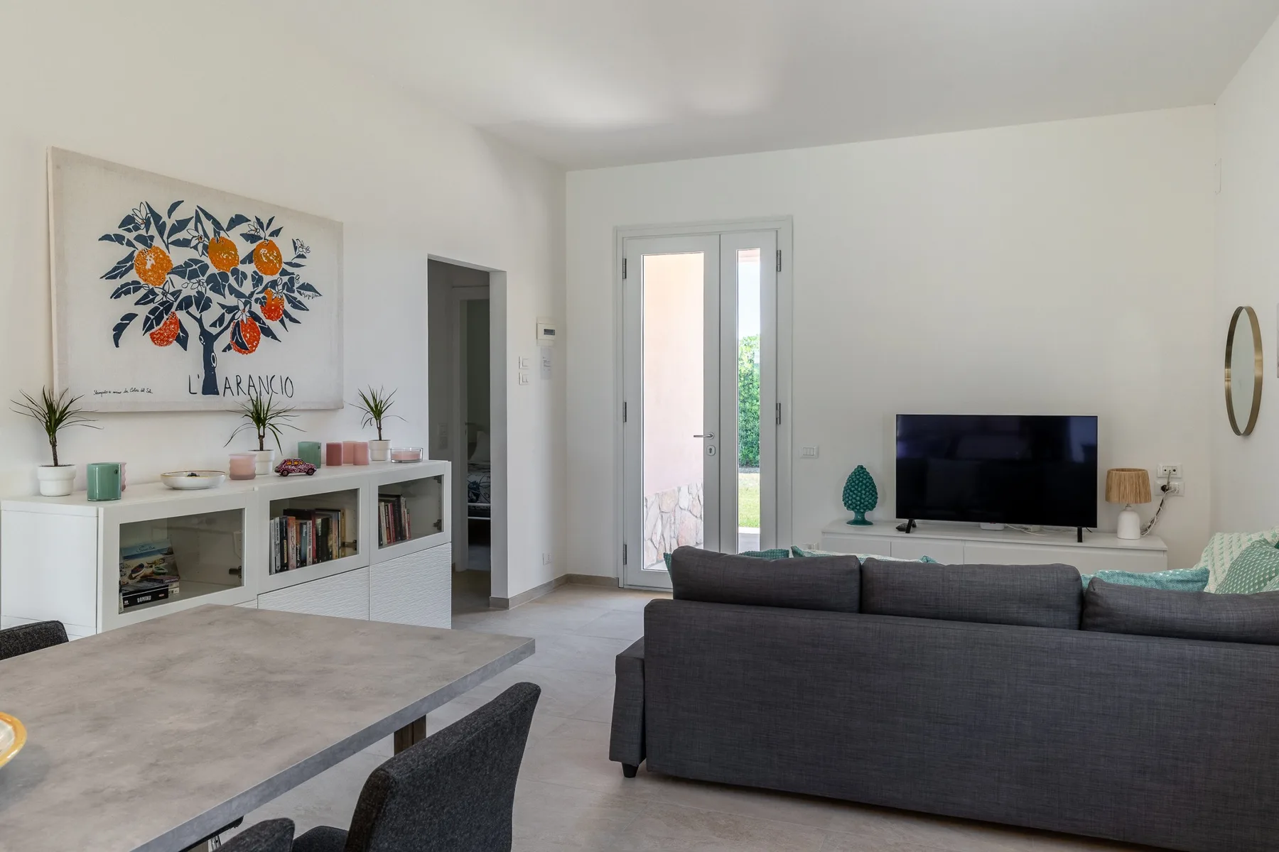 Una sala luminosa con un sofá oscuro, televisor y puertas de vidrio.