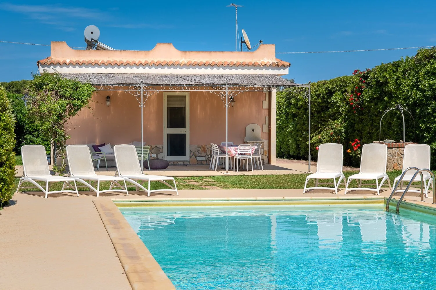 Una piscina y tumbonas están junto a una casa pequeña con un patio cubierto.