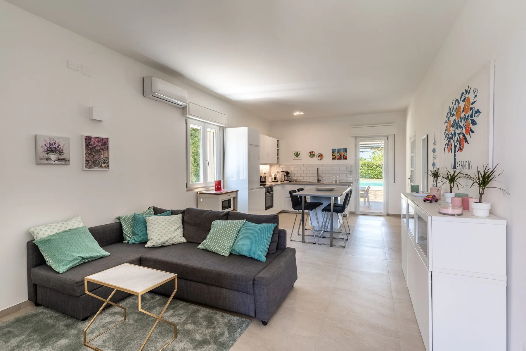 Un salón y cocina diáfanos y luminosos, con un sofá seccional gris y una mesa de comedor.