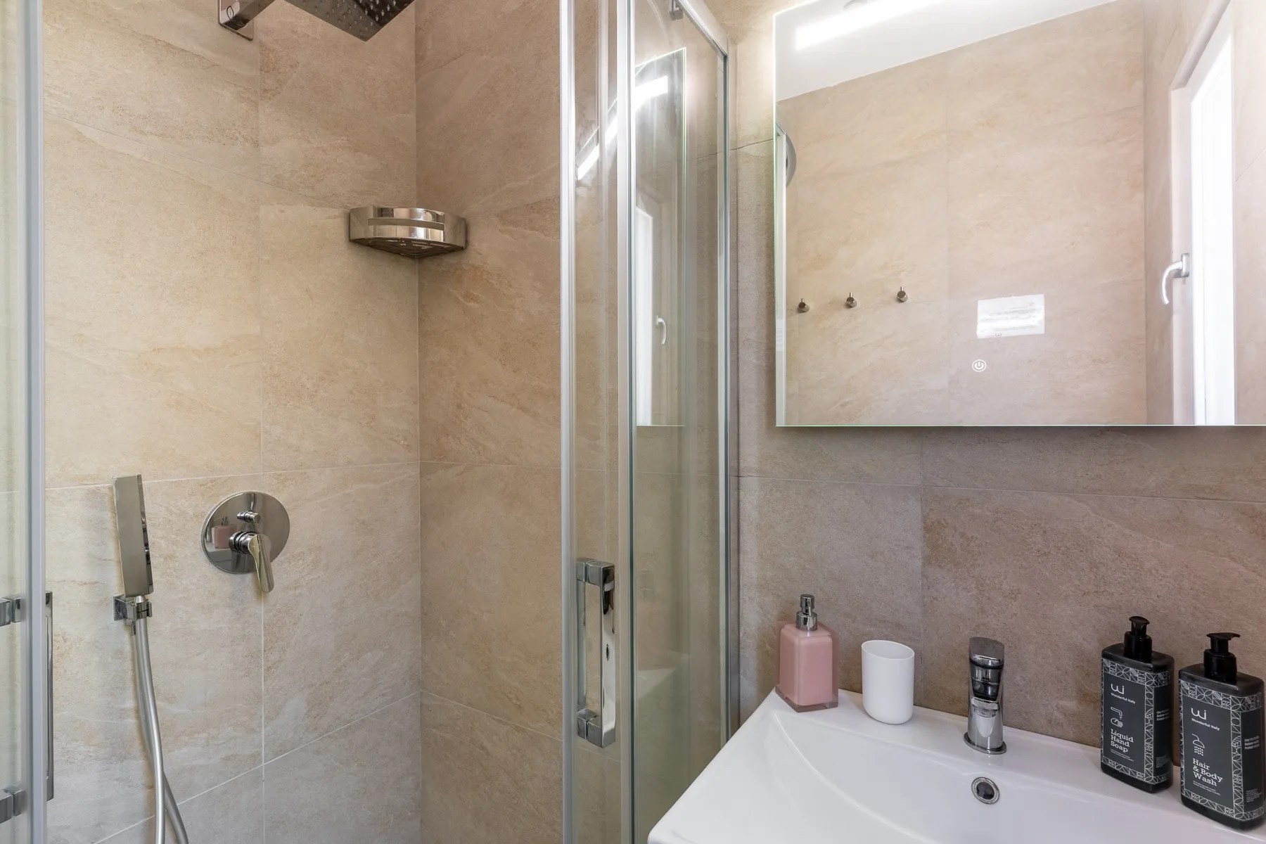 Un baño alicatado con una ducha de vidrio y un lavabo bajo un espejo.