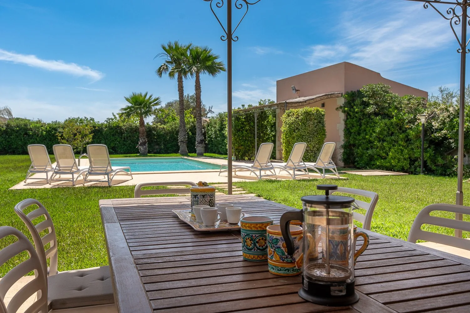 Un patio soleado da a un césped, una piscina y asientos de jardín.