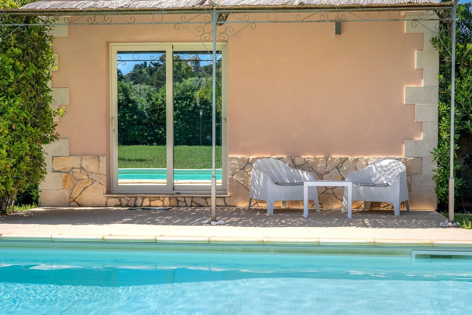 Una piscina junto a un patio con asientos al aire libre frente a una pared color durazno.