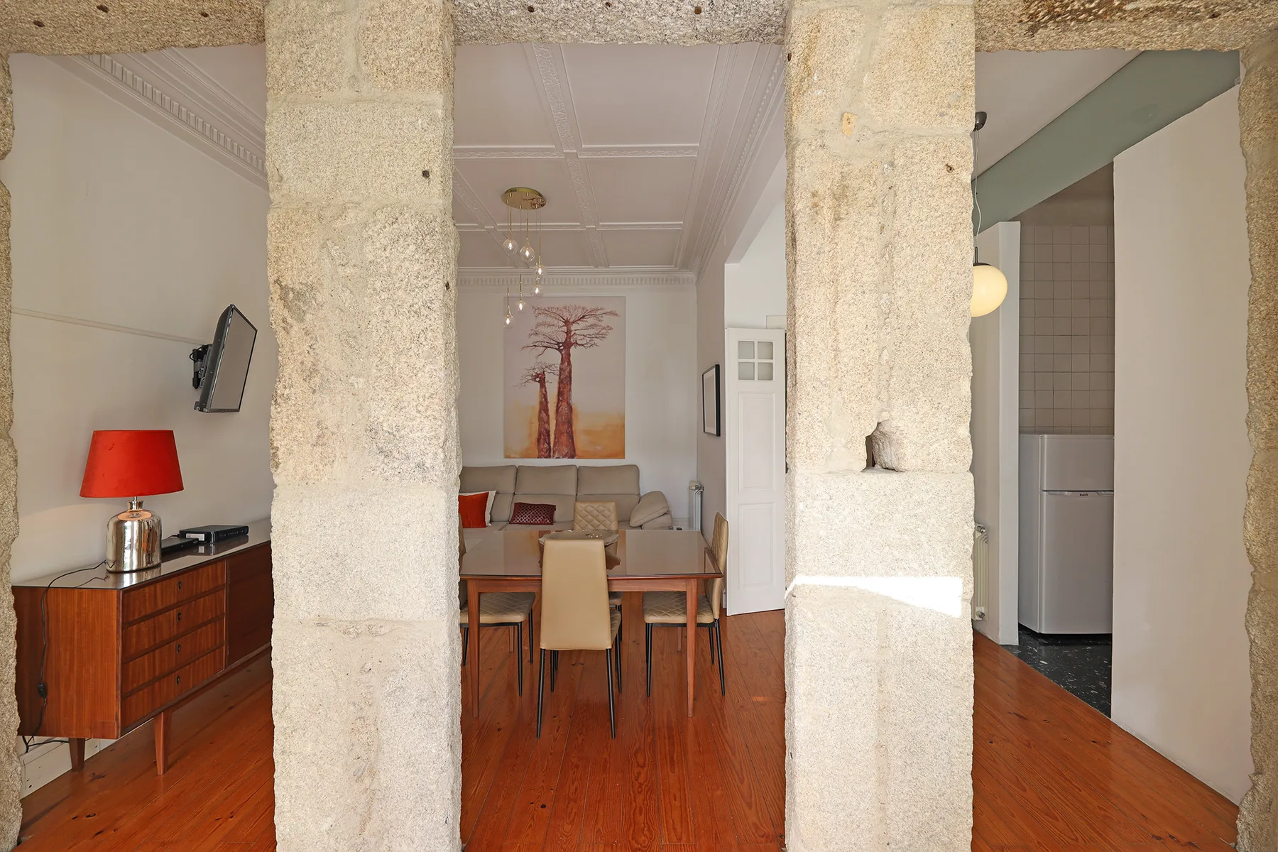 A dining area with a table and chairs sits between stone pillars in a bright apartment.