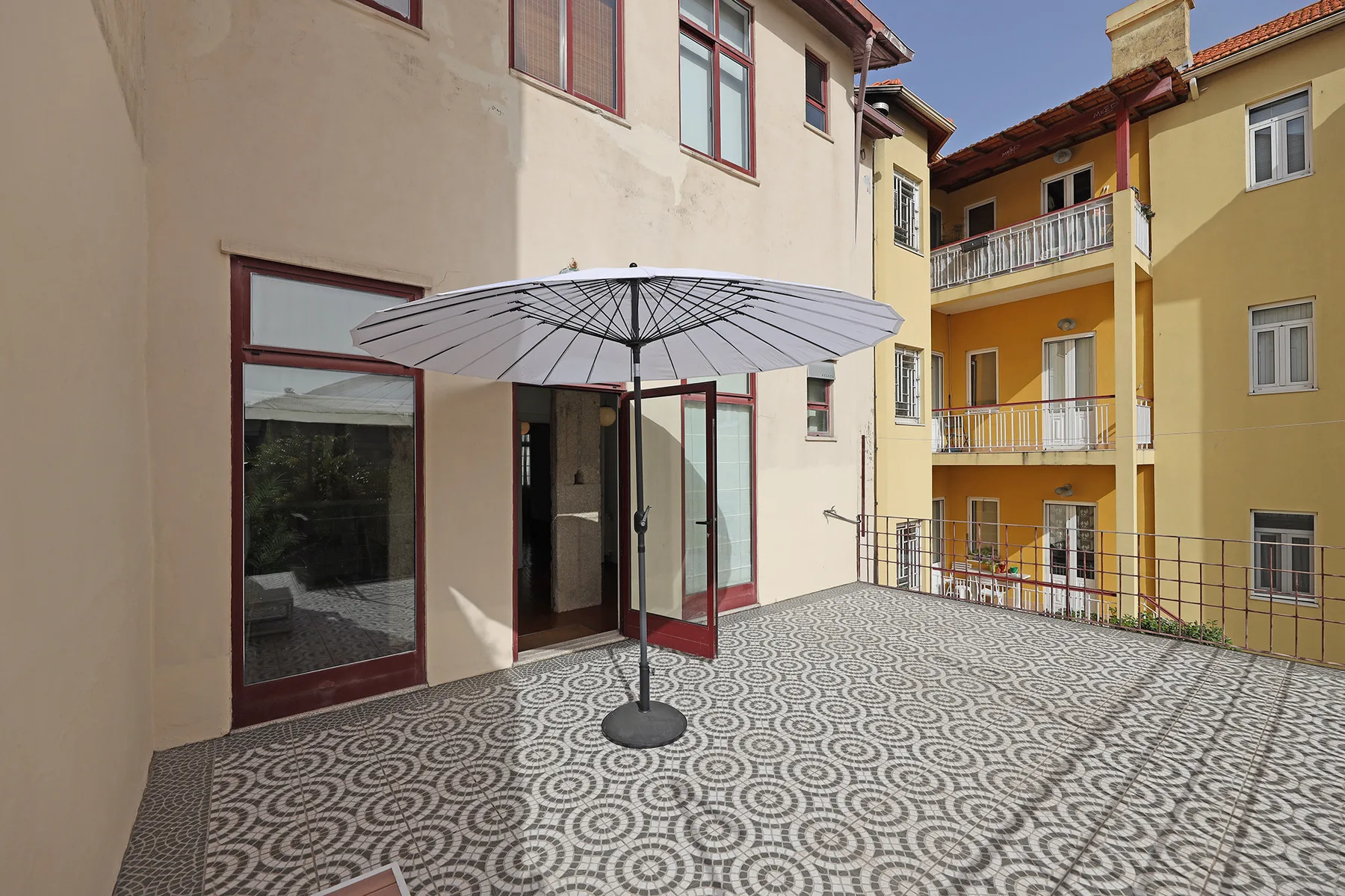 Una terraza exterior embaldosada junto a edificios de apartamentos, con una sombrilla abierta.