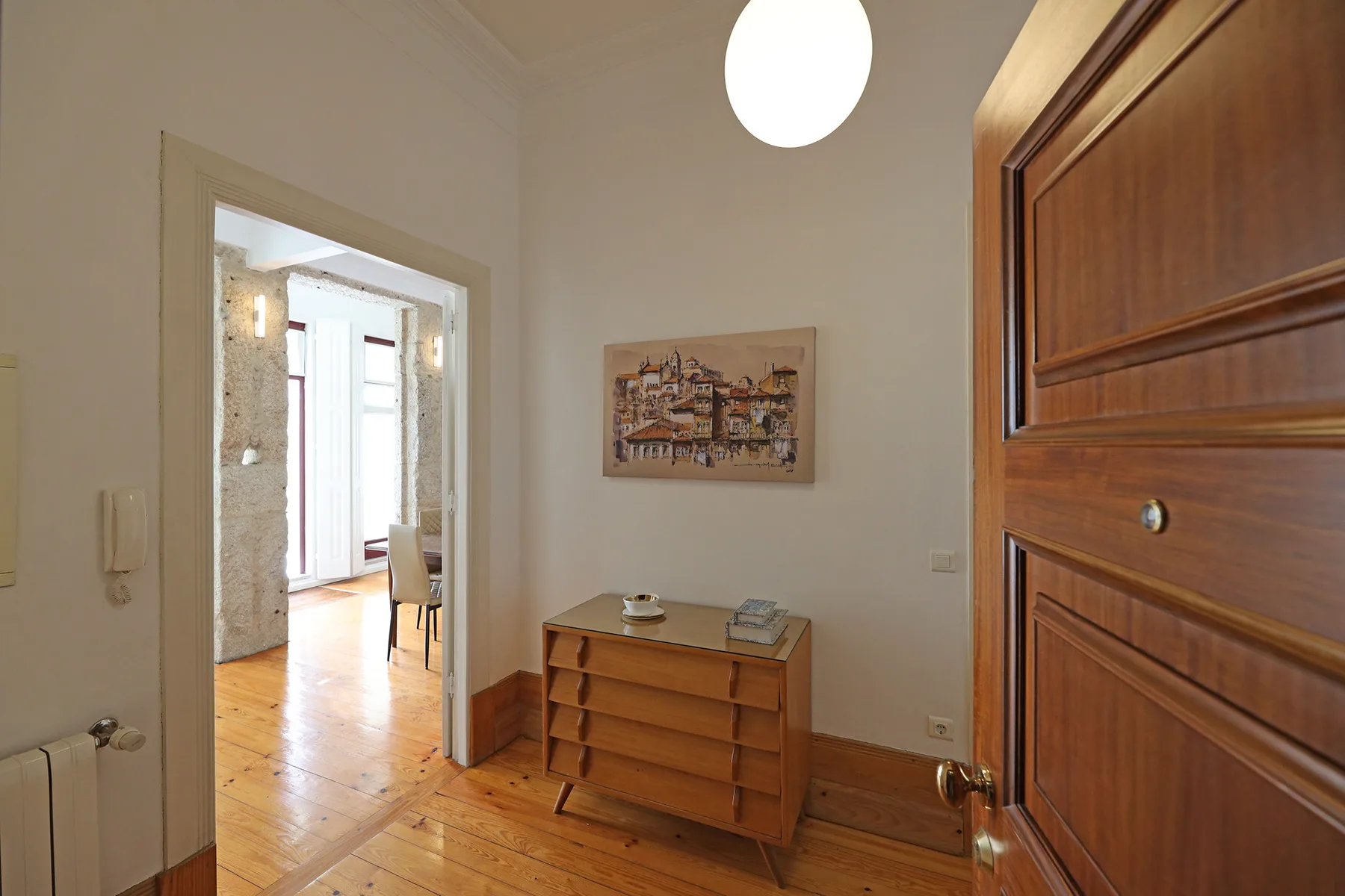 Entrada de un apartamento con una cómoda de madera y una puerta abierta a una habitación luminosa.