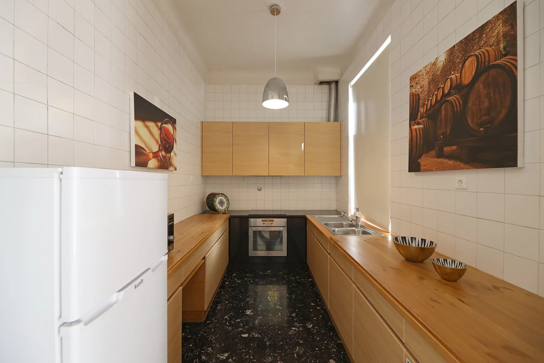 Una cocina estrecha con armarios de madera, un frigorífico y una encimera oscura.