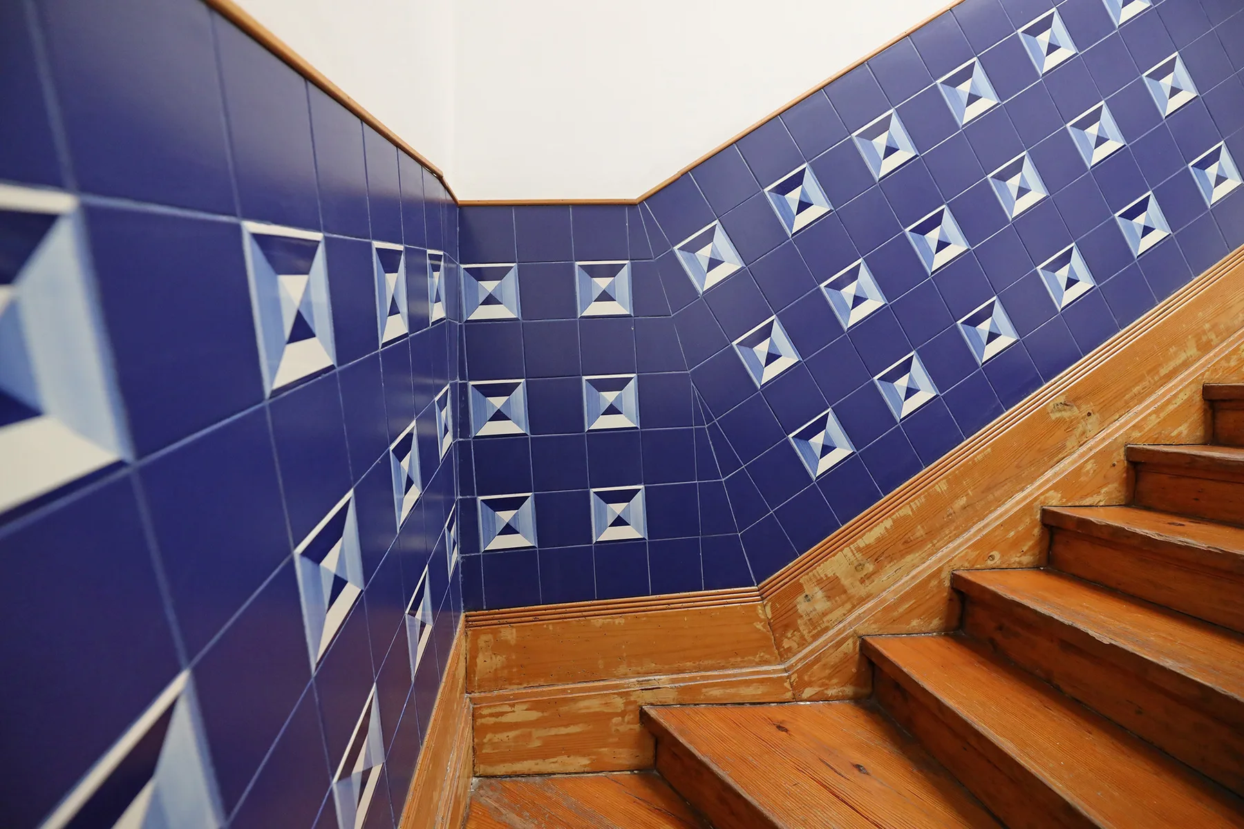 Una escalera de madera sube junto a paredes de azulejos azules estampados.