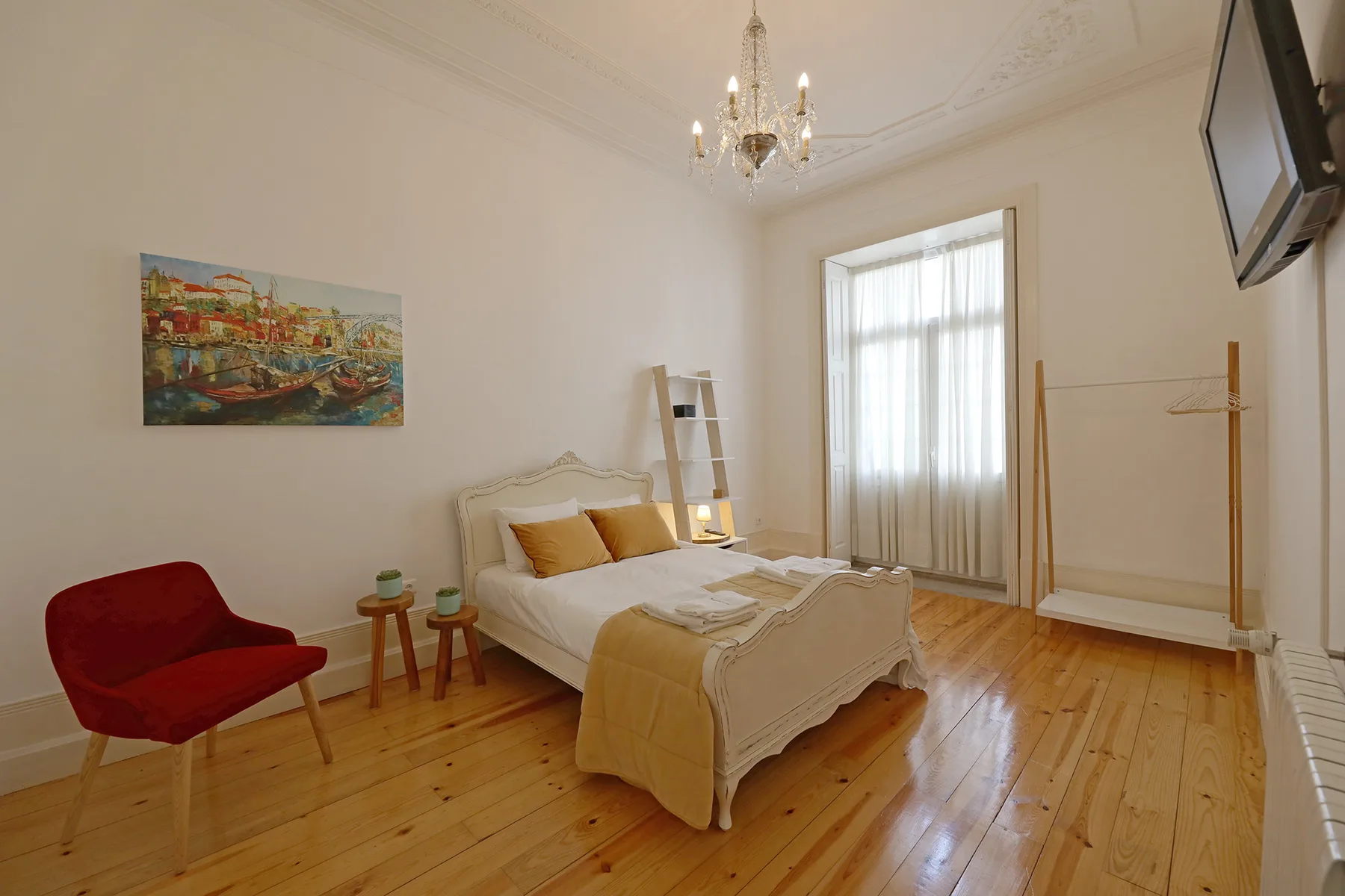 Un dormitorio con una cama, un asiento rojo y una ventana alta con cortinas.