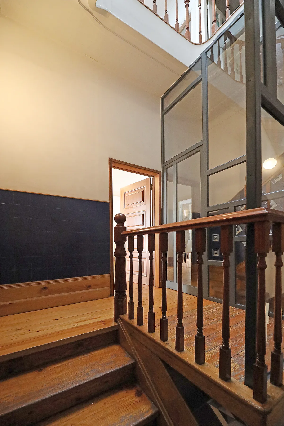 Una escalera interior con peldaños de madera y una barandilla oscura junto a un tabique de vidrio.