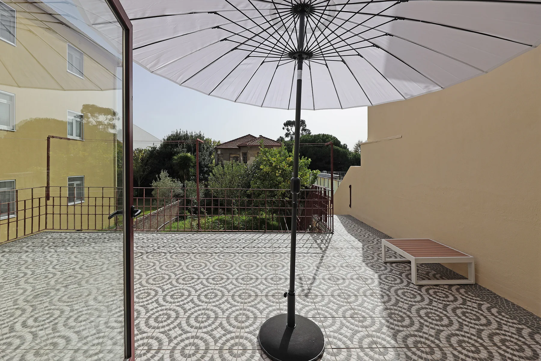 Una terraza de baldosas con una sombrilla grande y un banco bajo.