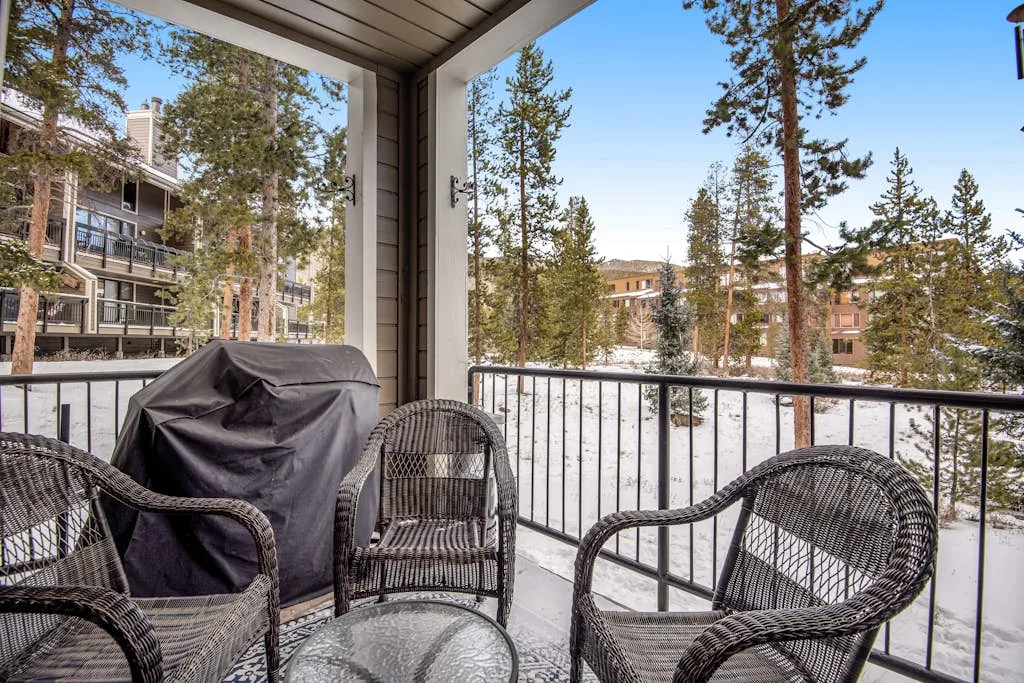 A covered balcony has wicker seating and a view of snow-covered ground and trees.