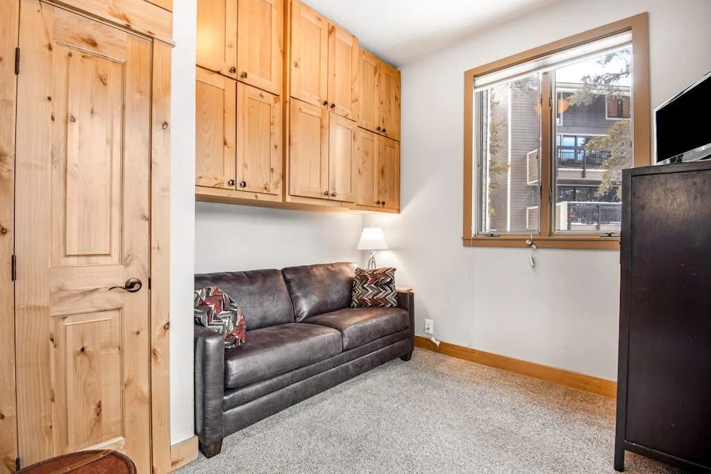 A compact living area with a dark sofa beneath wooden cabinets and a window.