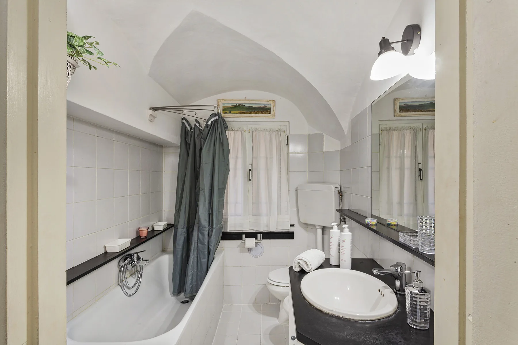 Un baño alicatado con bañera, cortina de ducha, inodoro y lavabo.
