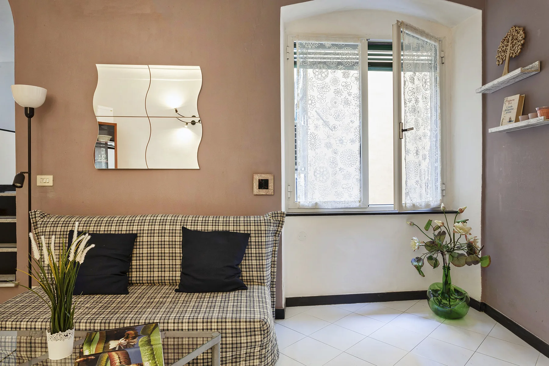 Sala de estar con sofá a cuadros, espejo de pared y una ventana luminosa.